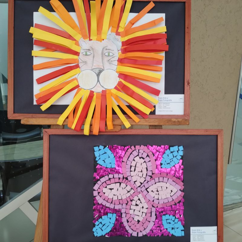 Dos trabajos enmarcados sobre un atril: un león con melena de tiras de papel naranja y un mosaico de papel rosa