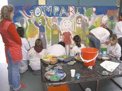 Estudiantes de guardapolvo blanco pintan un mural con la palabra Compartir